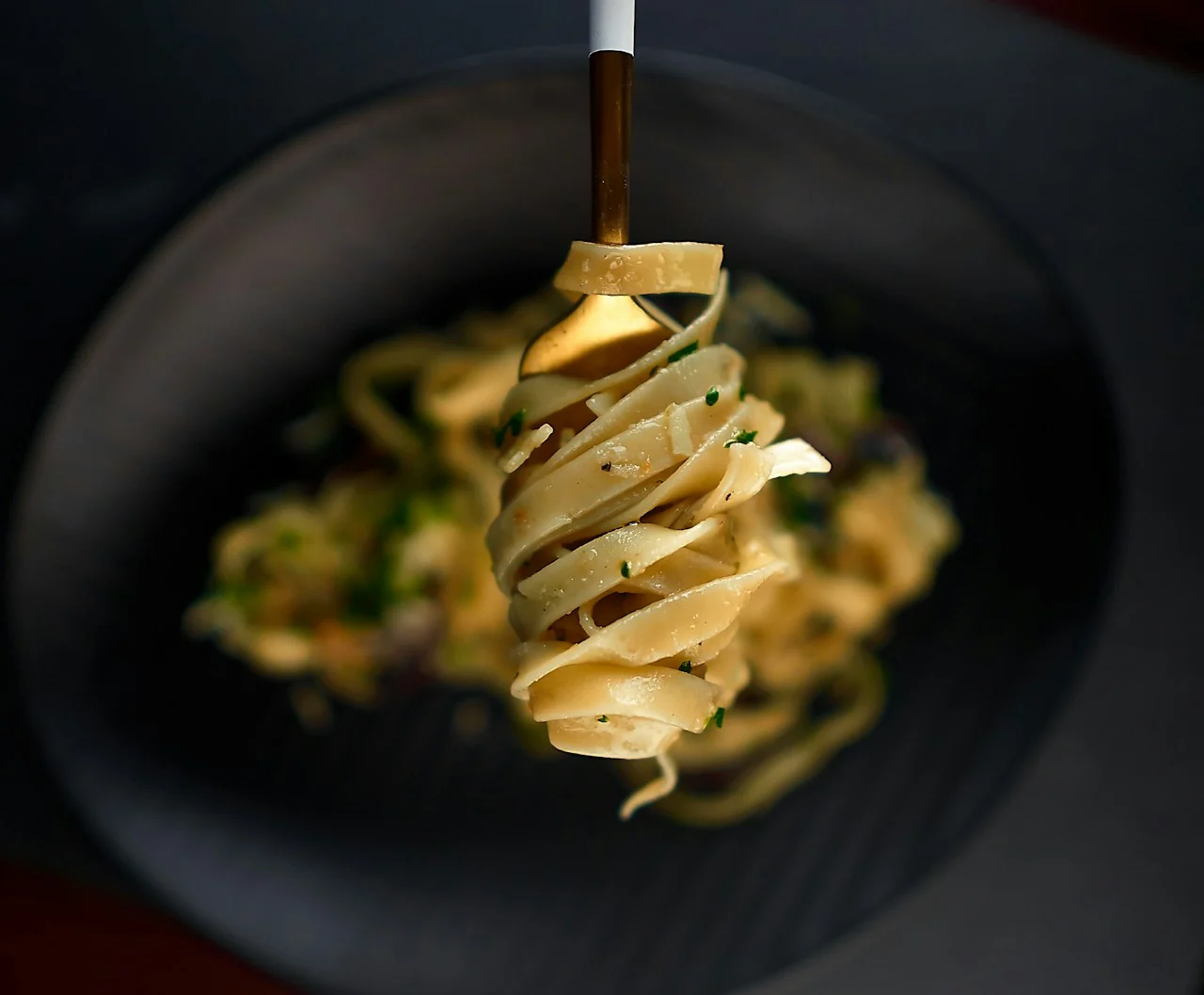Golden mushroom pasta lifted on a fork above a black ceramic plate