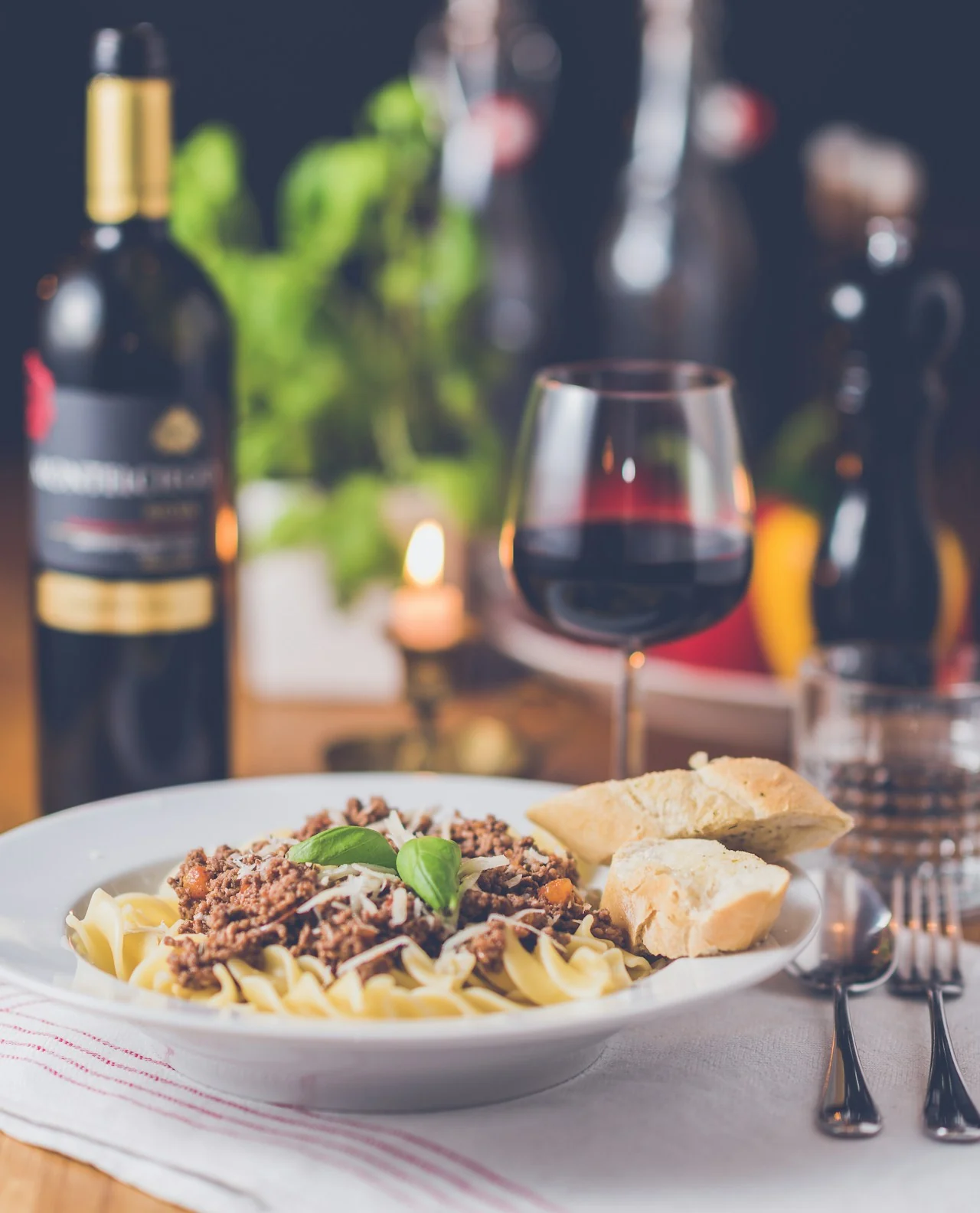 Pasta with meat sauce, a glass of red wine and a candle on a dining table