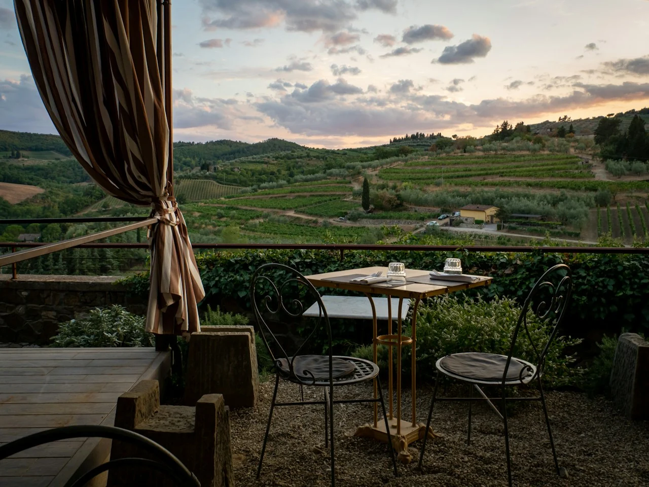 A table for two on a shaded terrace overlooking vineyards and Tuscan hills at sunset