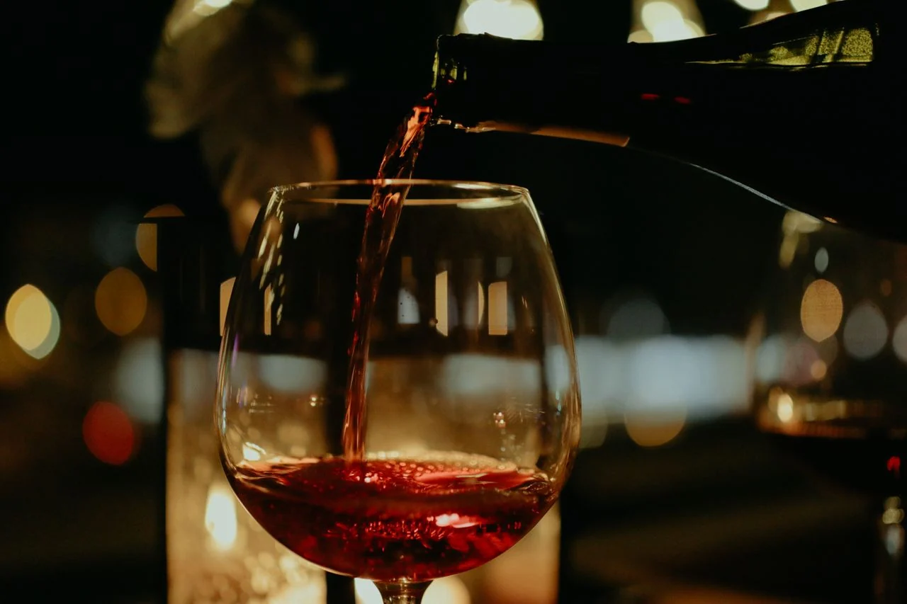 Red wine being poured from a dark bottle into a clear wine glass against warm blurred lights