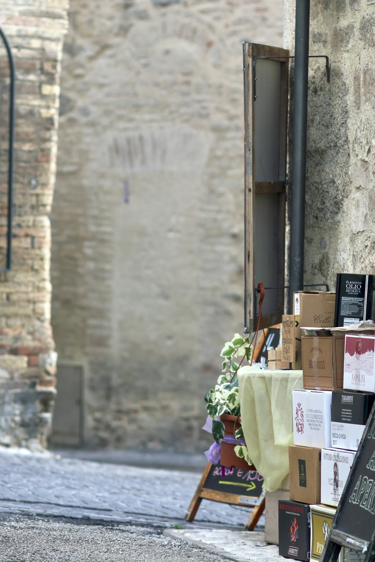 Wine cartons and an olive oil display beside a stone lane in Montefalco