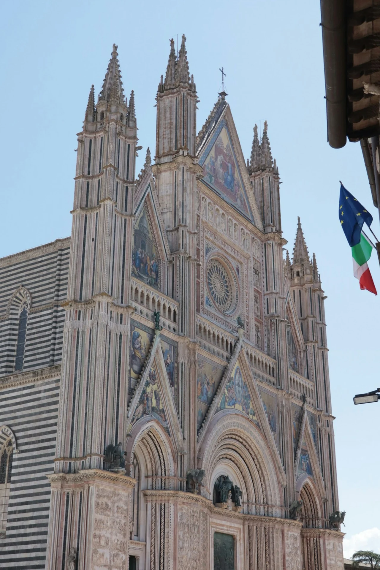 The ornate mosaic facade and striped stone side of Orvieto Cathedral beneath a blue sky