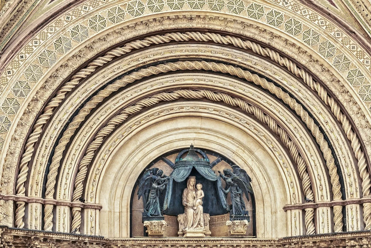Sculpture of the Madonna and Child beneath richly carved arches above an Orvieto cathedral doorway