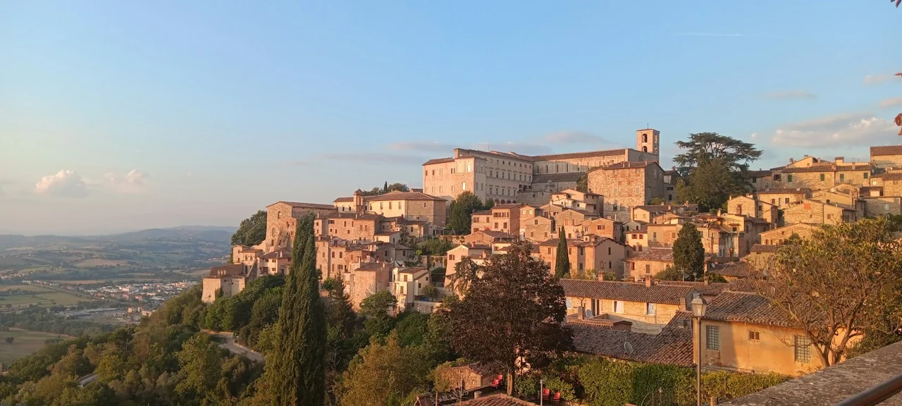 Stone houses and the bell tower of Todi above the Umbrian valley in warm evening light