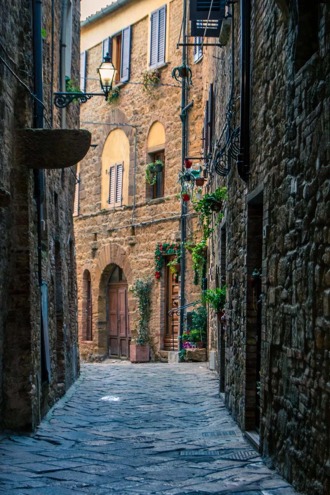 A stone lane in Volterra with an illuminated lantern and plants beside the doorways