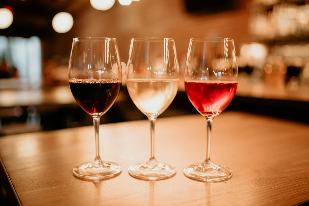 Three glasses of wine on a wooden table, with warm golden light in the background.